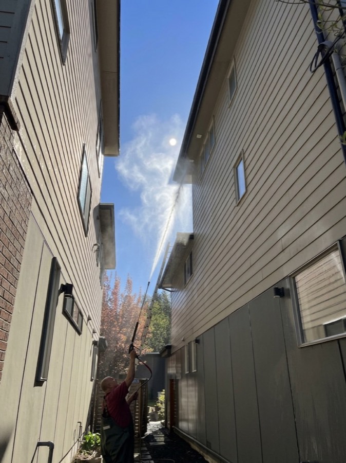 3 Amigos crew member pressure washing home siding between houses